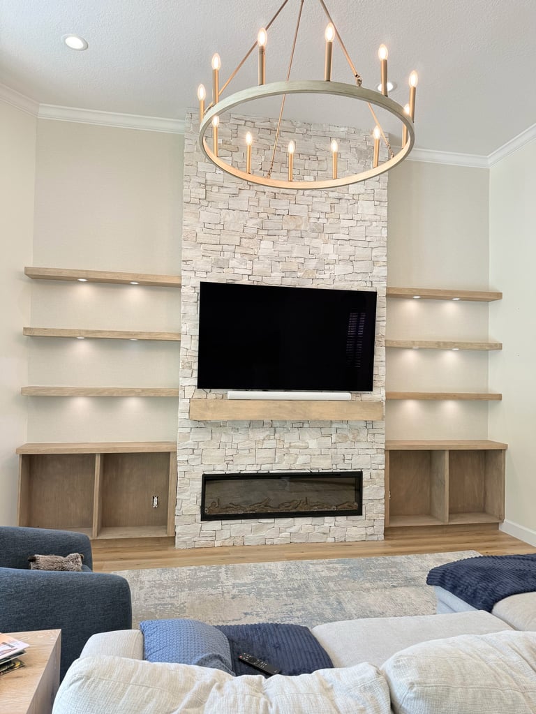 Modern living room with fireplace, mounted TV, floating shelves, and a circular chandelier above white stone accent wall