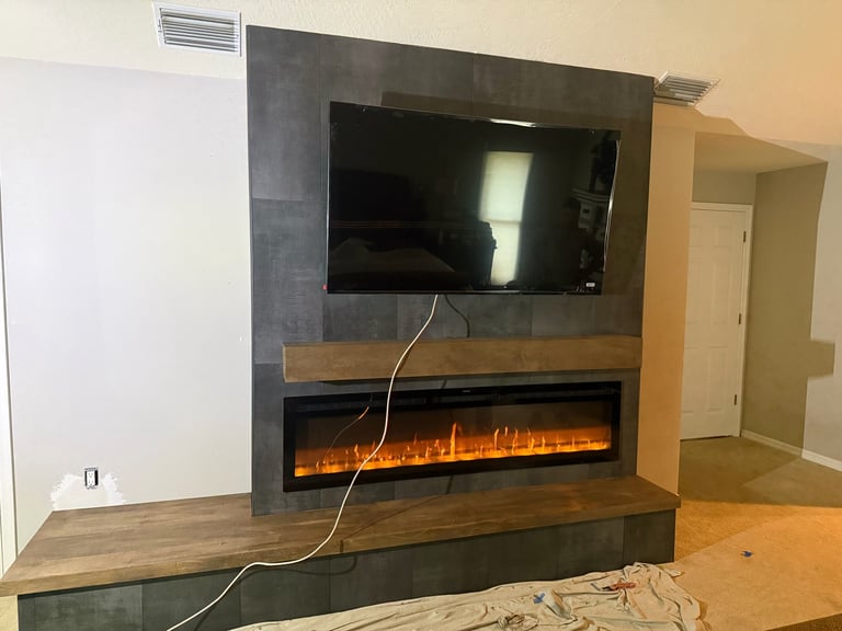 Modern living room with flat-screen TV mounted above an electric fireplace insert in a dark stone and wood feature wall