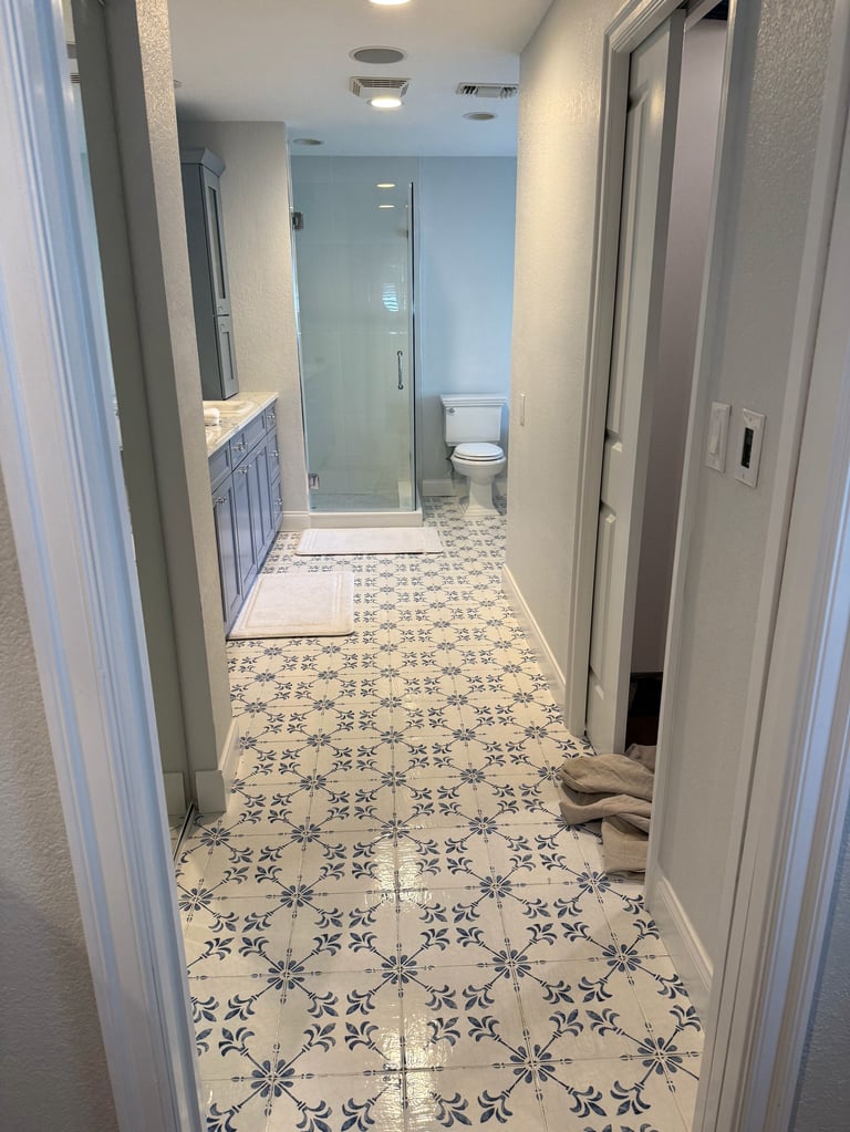 Modern bathroom hallway with patterned tile floor, glass shower enclosure, toilet, sink vanity, and white cabinetry